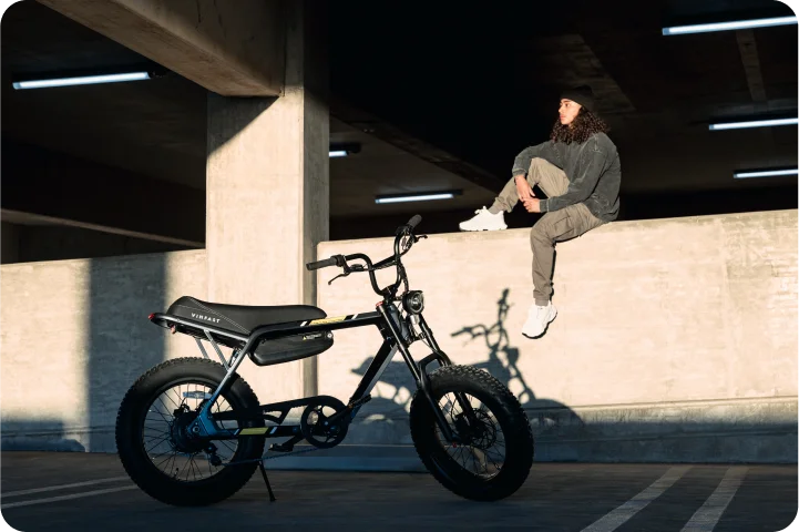 A VinFast electric bike is parked in a parking garage with a man sitting on the ledge behind it