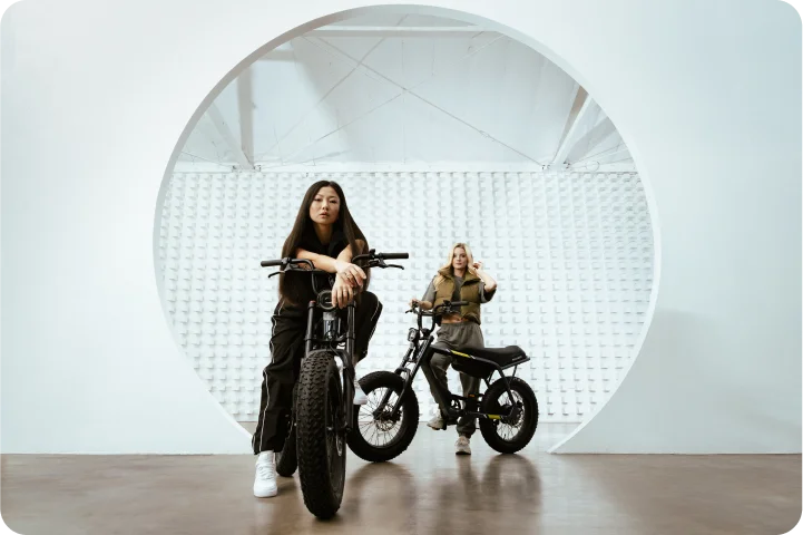 2 girls pose with the VinFast electric bike in a white room, one sitting, one standing