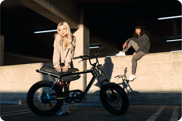 A blonde girl leans onto her VinFast electric bike with a guy sitting on the ledge behind her