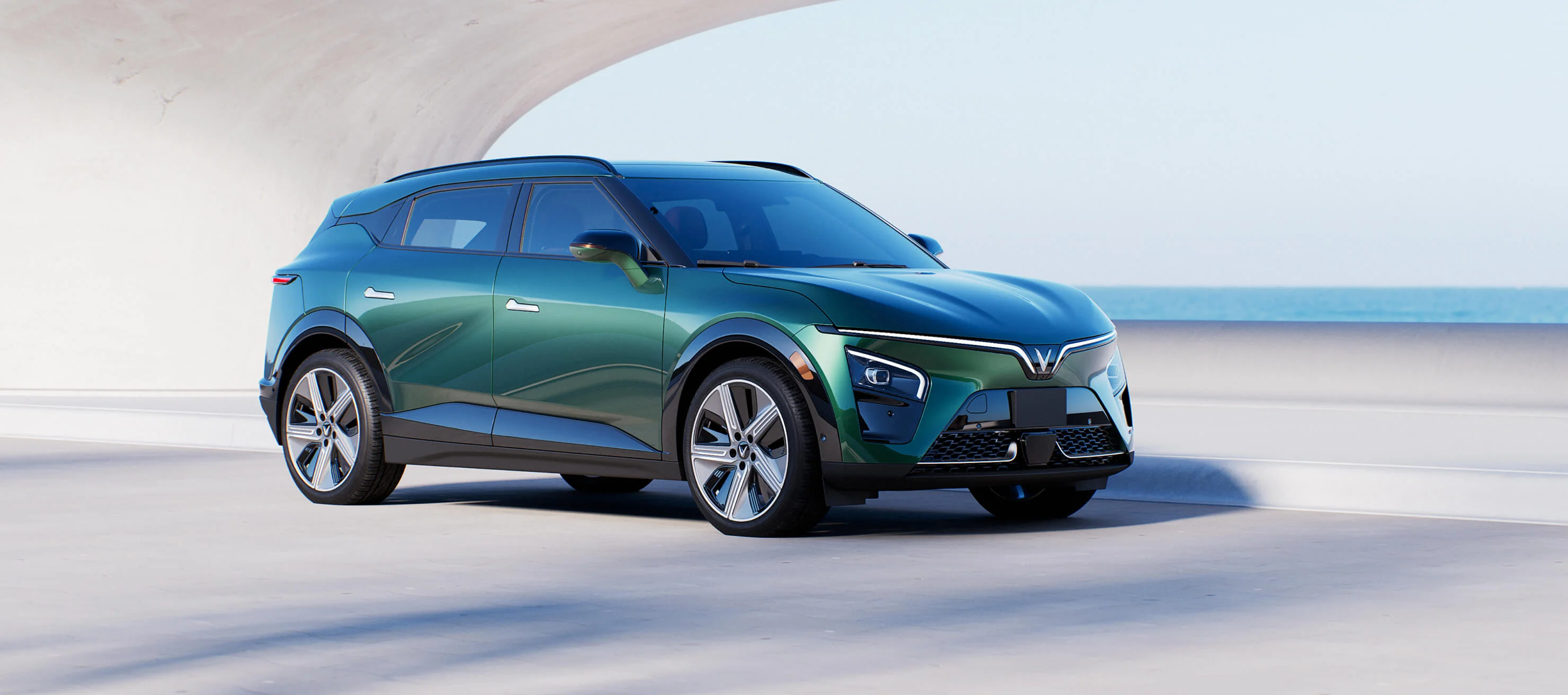 A Deep Ocean Green VF 7 is parked on the road near the beach on a sunny day