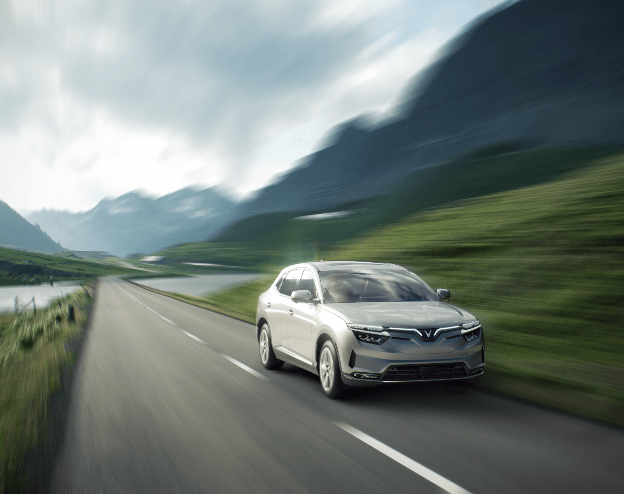 A silver VF 8 is driving fast down the road through mountainous terrain