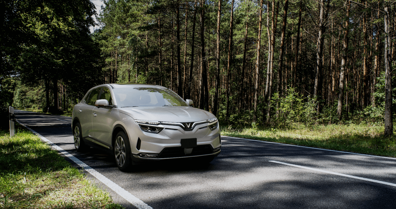 A silver VF 8 is driving down a shady, wooded road